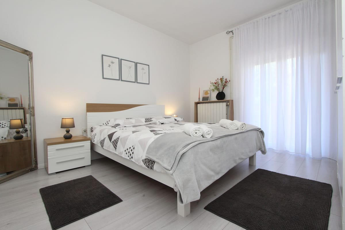 Une chambre moderne avec un lit, des tables de chevet, un miroir et une fenêtre avec des rideaux.