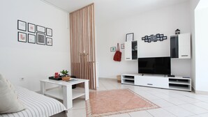 A modern living room with a sofa, a coffee table, a TV, and a wall-mounted TV stand. - Apartments Rozi (Rovinj)