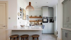 A kitchen with a central island, bar stools, a hanging light fixture, and a microwave.