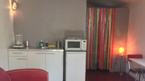 Un espacio habitable compacto con kitchenette, un sofá rojo y una cortina colorida.
