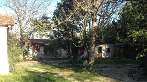 Un espacio rústico al aire libre con un sendero de tierra, una bicicleta y un edificio con ventanas rojas y techo de tejas.