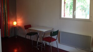 Una habitación con una mesa blanca y dos sillas, un radiador y una ventana que da a zonas verdes.