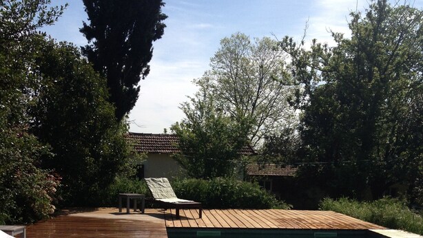 Una terraza de madera que conduce a una piscina cristalina con sillas de descanso y una pequeña mesa.