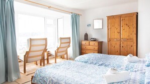 A bedroom with a bed, two chairs, a wooden wardrobe, and a dresser.