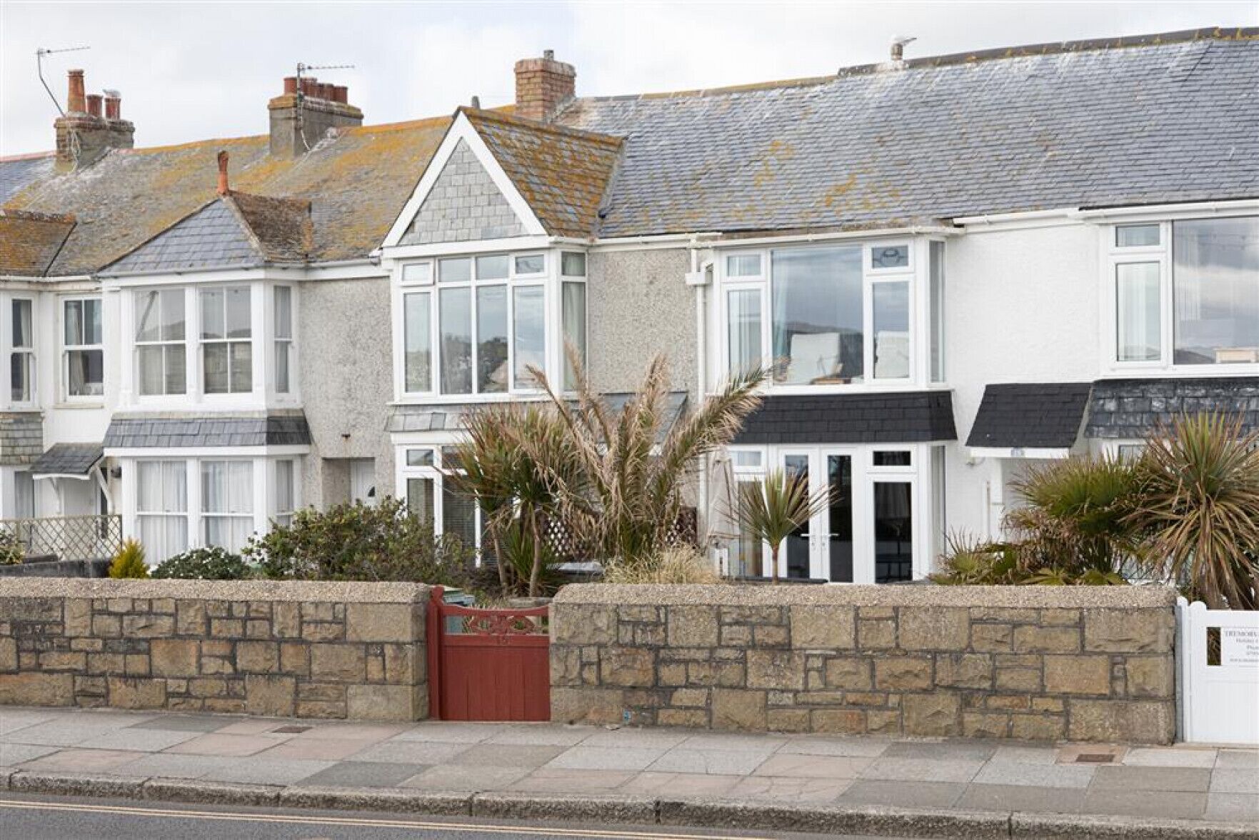 A row of terraced houses with stone walls, a red gate, and a paved sidewalk.