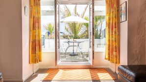 A room with a sliding glass door leading to an outdoor area with a table and chairs, a black leather sofa, and a patterned rug.