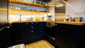 A modern kitchen with dark cabinetry, wooden shelves, and stainless steel appliances. - Sinclair Sophistication, by Veeve (London)