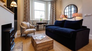 A living room with a dark blue sofa, a patterned armchair, and a wooden chest of drawers. - Sinclair Sophistication, by Veeve (London)