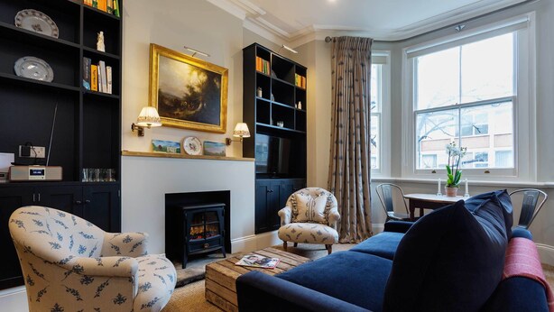 A living room with a fireplace, a sofa, a chair, and a bookshelf. - Sinclair Sophistication, by Veeve (London)