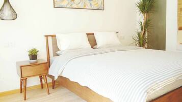 Un dormitorio con cama de madera, ropa de cama blanca, una mesita de noche con una planta y una lámpara colgante.