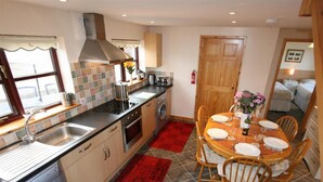 A compact kitchen with a stove, sink, and a dining area with a table set for four. - Skylark - Three Bedroom Cottage, Sleeps 6 (Camborne)