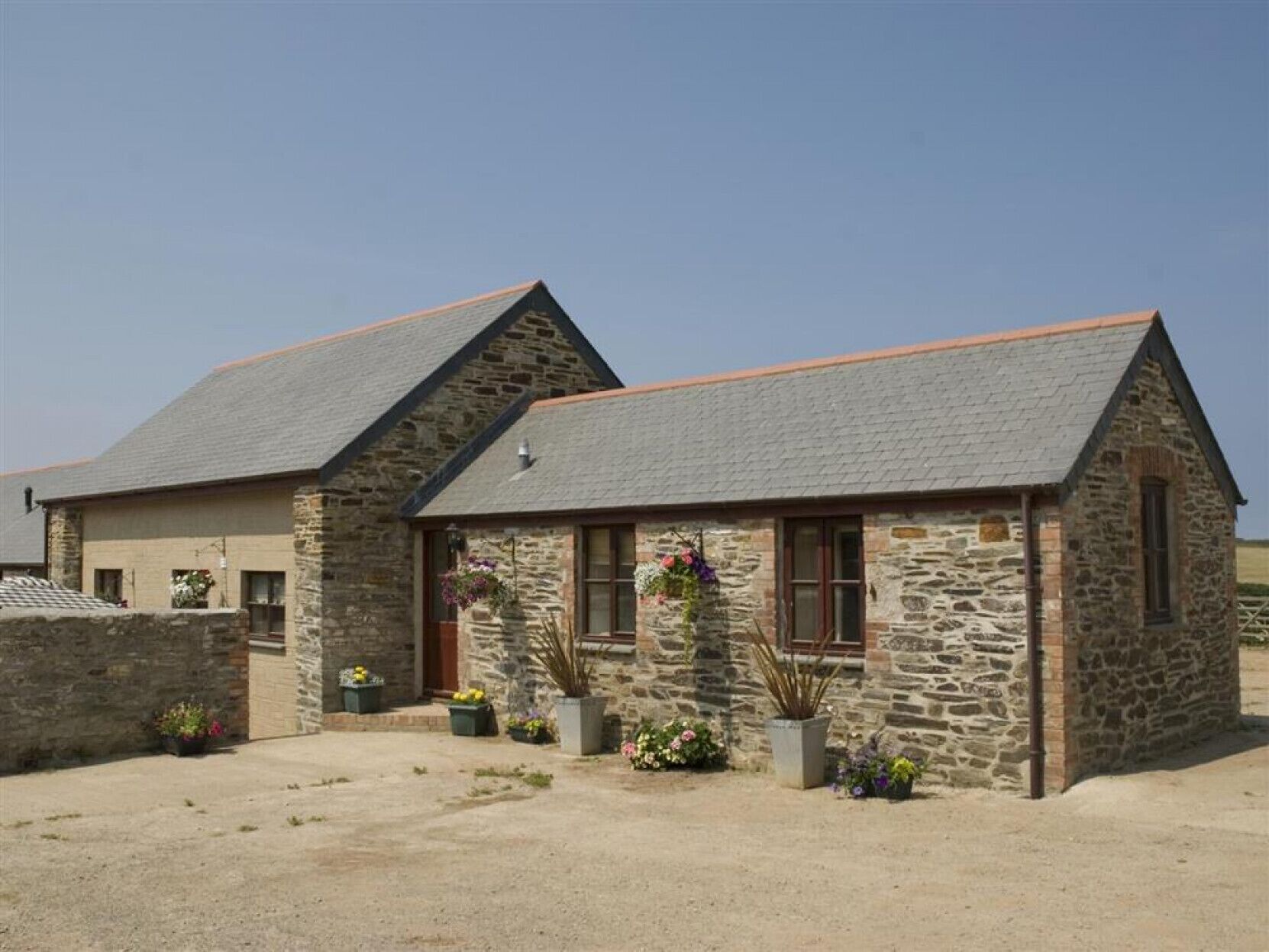 A stone building with a sloped roof, a front entrance, and potted plants.