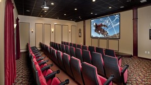 Un salón de conferencias con filas de sillas rojas y negras, una pantalla grande que muestra una imagen con temática espacial y una alfombra estampada.