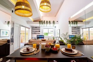 Un espace repas moderne avec une table mise pour le petit-déjeuner, des plantes suspendues et une vue sur l’extérieur.