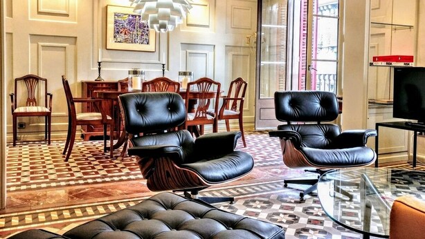 Een moderne woonkamer met een eethoek, met lederen fauteuils, een glazen salontafel en een vloer met een patroon.