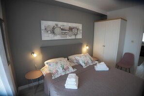 A neatly made bed with floral pillows, a bedside table with a lamp, and a large artwork on the wall. - Apartments San Francesco (Rovinj)