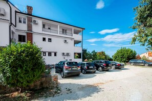Um edifício de dois andares com várias varandas e carros estacionados na frente.