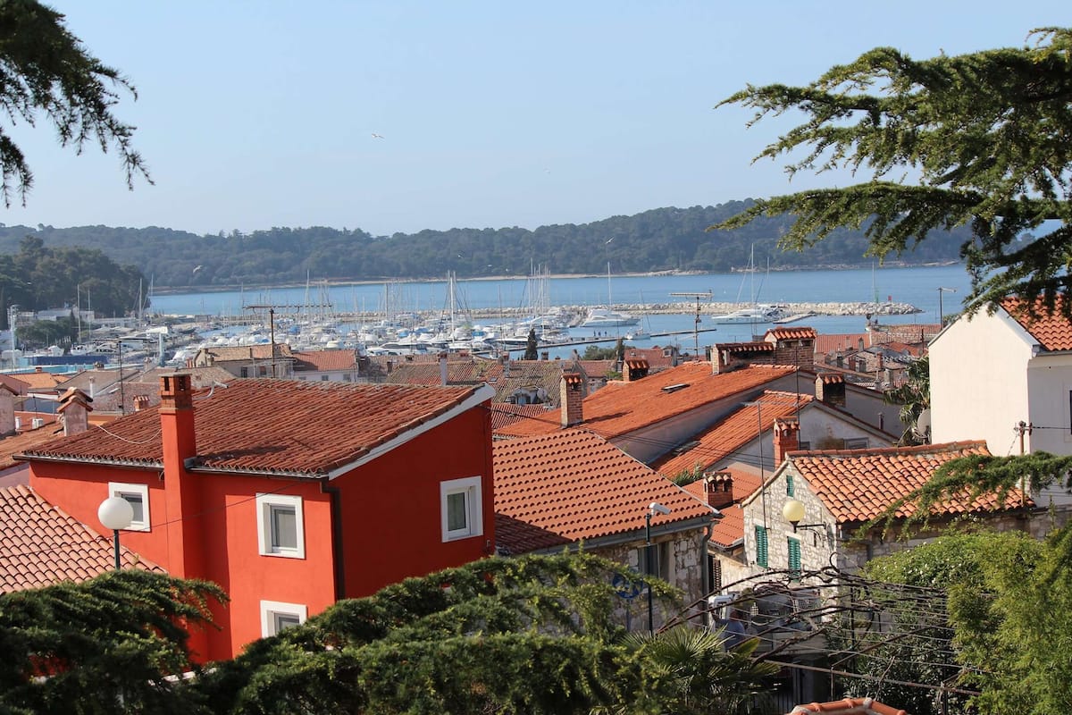 A coastal town with red-roofed buildings, a marina with boats, and a clear view of the sea.