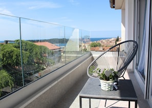 Un balcón con vista despejada a un pueblo costero, una planta en maceta y una silla.