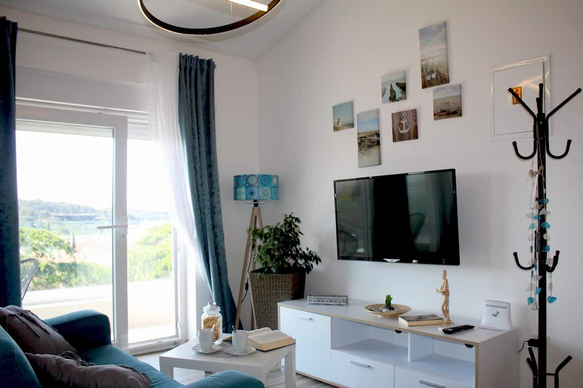 A modern living room with a large TV, a sofa, a coffee table, and a view of the outdoors.