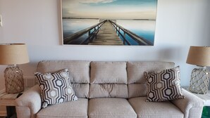 Un canapé beige agrémenté de coussins à motifs, une table basse en bois et un tableau encadré représentant une jetée.