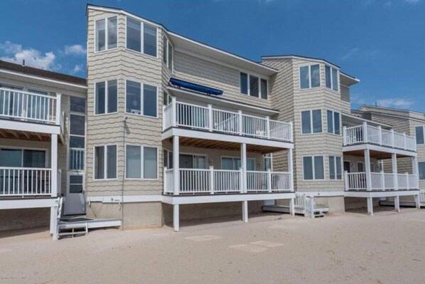 A beachfront hotel with multiple balconies, a covered outdoor area, and a sandy beach.