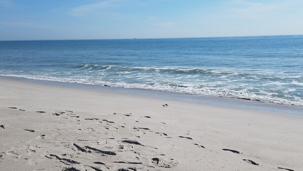 Une plage où l’on peut voir des empreintes de pas dans le sable et d’où la vue sur l’océan est dégagée.