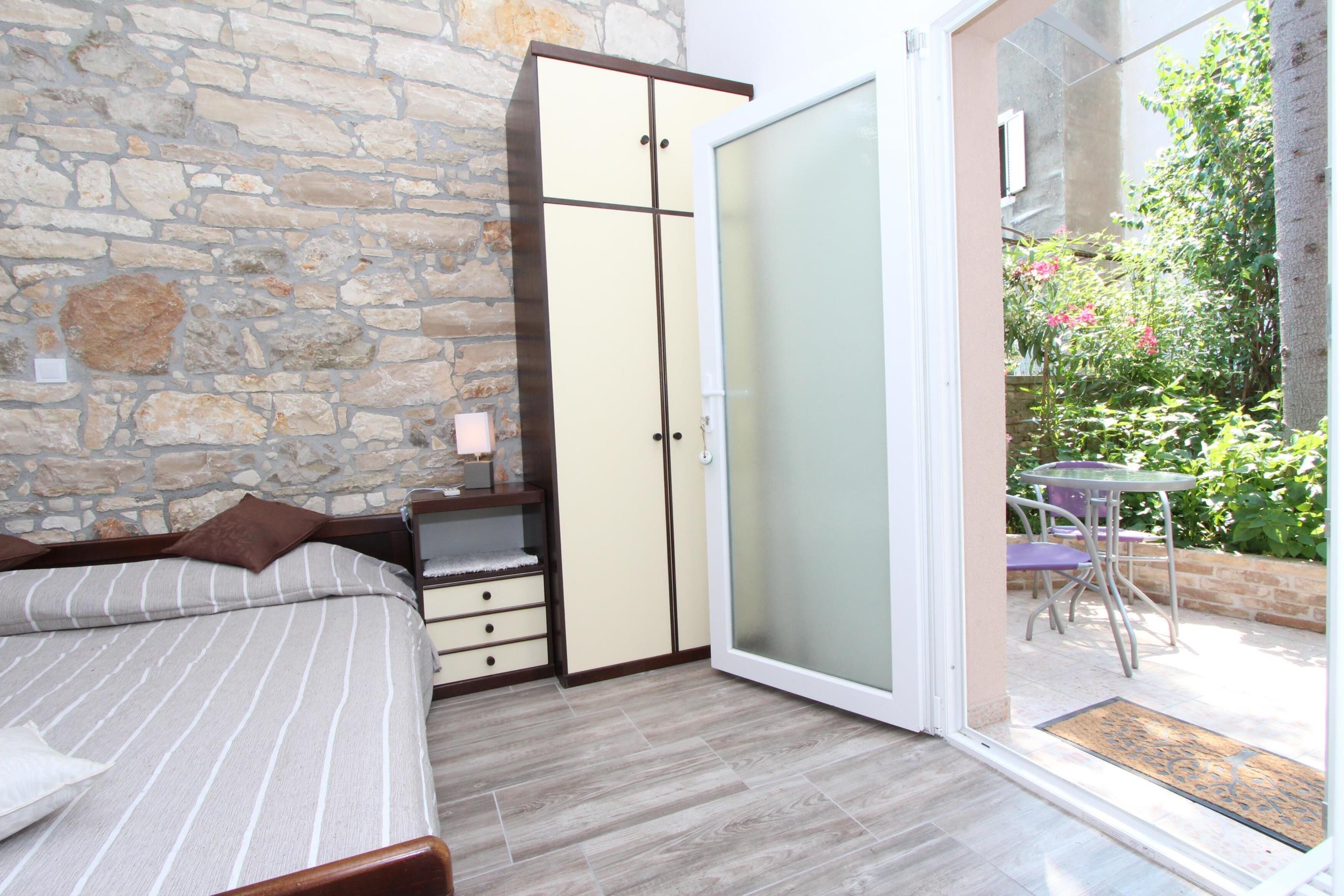 A bedroom with a bed, a wardrobe, and a sliding glass door leading to an outdoor patio with a table and chairs.