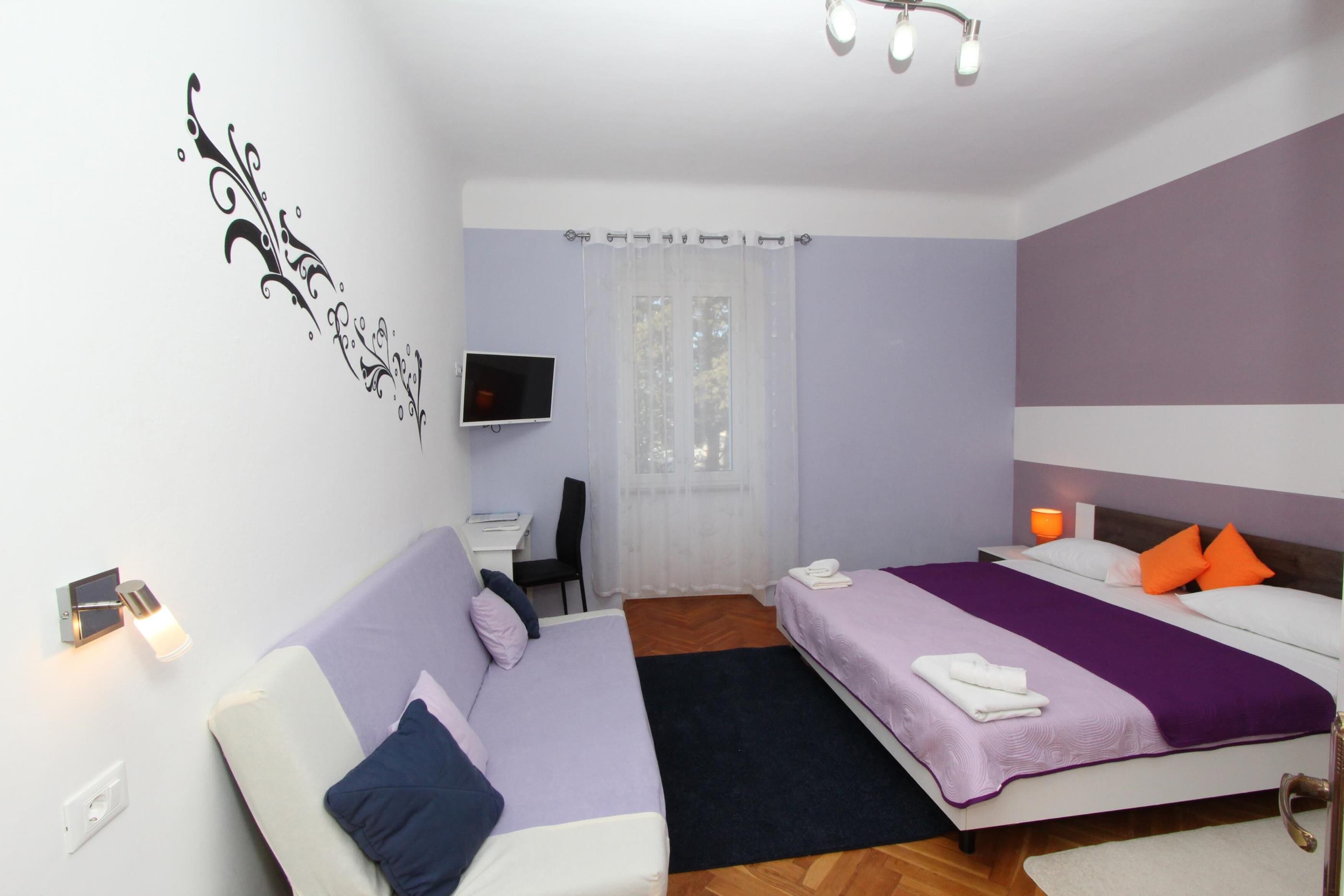 A hotel room with two beds, a desk, a TV, and a window with curtains.