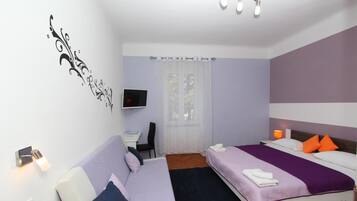 A hotel room with two beds, a desk, a TV, and a window with curtains.