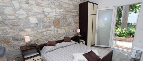 Un dormitorio con pared de piedra, una cama con ropa de cama a rayas, un armario y un ventanal corredero que da a un jardín.