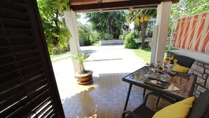 An outdoor patio area with a table and chairs, a potted plant, and a view of a garden and street. - Studio Sea (Rovinj)