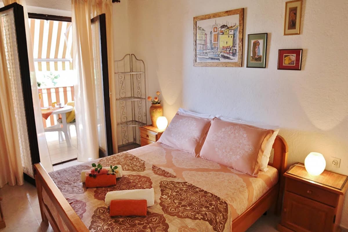 Une chambre à coucher avec un lit, des tables de chevet, une commode, une chaise et une fenêtre avec des rideaux.