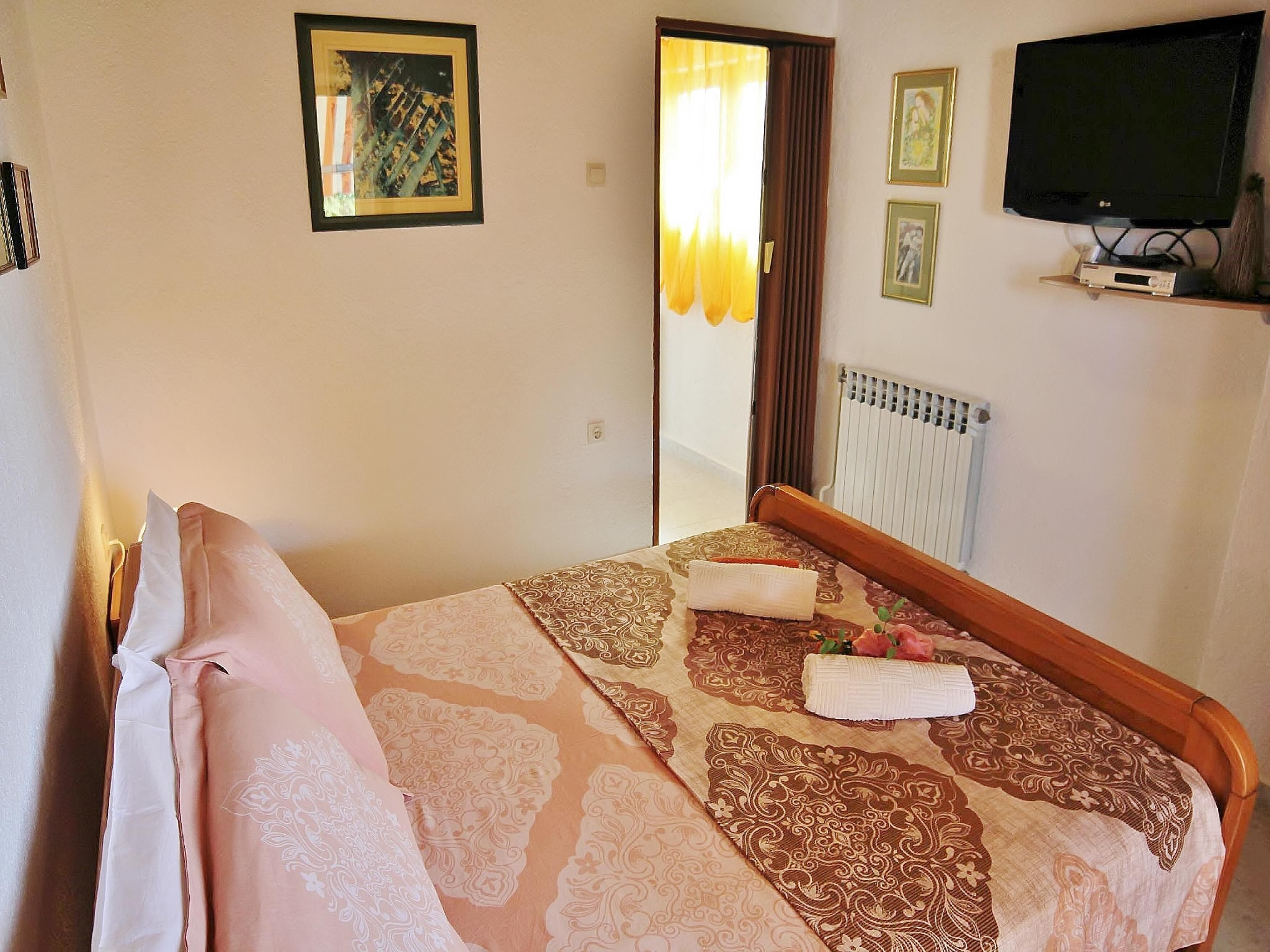Een keurig opgemaakt bed met behang, een televisie op een standaard en lijstwerken aan de muur.