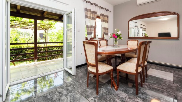 A dining area with a table and chairs, a large mirror, and a view of greenery through an open door. - Apartments Sena (Rovinj)