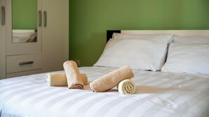A neatly made bed with white and beige striped bedding, a green wall, and a white wardrobe with silver handles. - Apartments Sena (Rovinj)