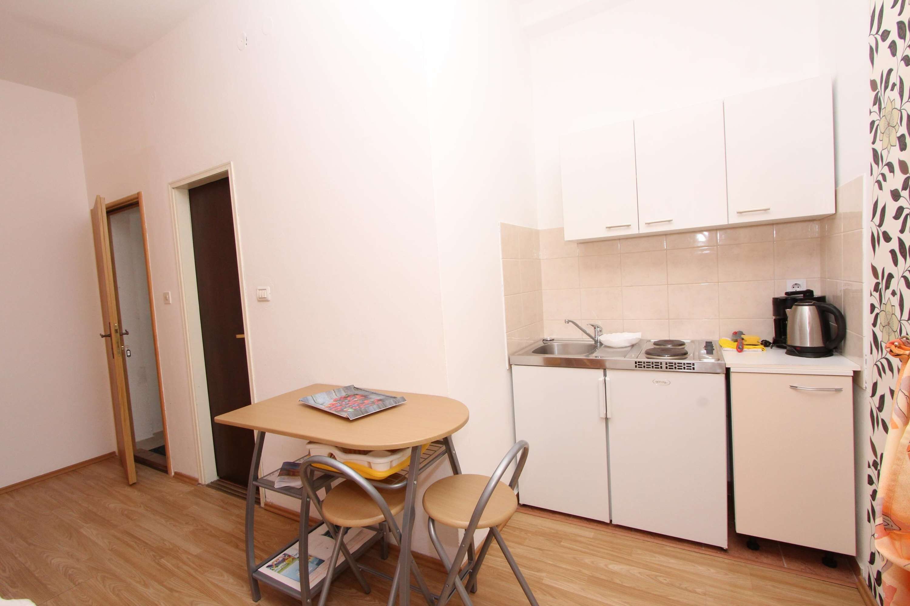 A compact kitchen with a small dining table and chairs, a refrigerator, a stove, and a sink.