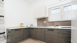 A modern kitchen with grey cabinets, a white countertop, and a window with curtains. - Apartments Sena (Rovinj)