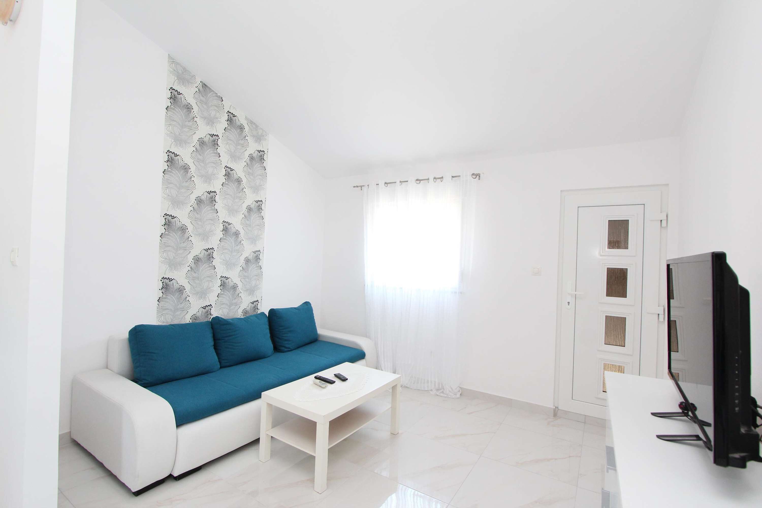 A white living room with a sofa, a coffee table, a TV, and a door.