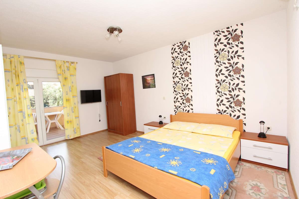 A bedroom with a bed, a desk, a wardrobe, a TV, and a window with curtains.