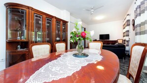 A dining area with a wooden table, chairs, a vase with flowers, and a television in the background. - Apartments Sena (Rovinj)