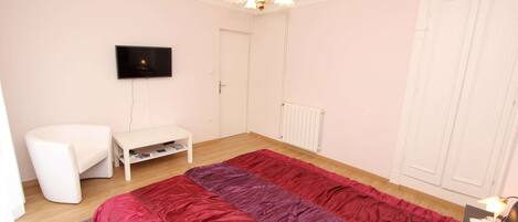 A bedroom with a bed, a TV, a chair, a small table, and a wardrobe.