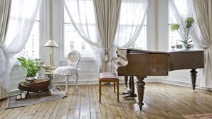 A room with a grand piano, a chair, a small table with a plant, and a lamp.
