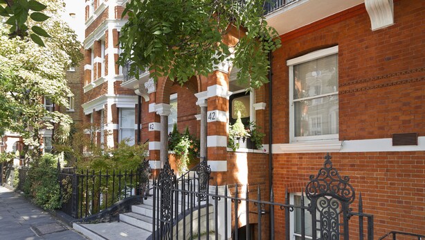 A row of red brick townhouses with white trim, numbered 42 and 43, featuring a black wrought iron fence and a small garden area.