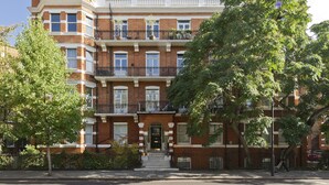 A multi-story brick building with a central entrance, multiple windows, and a balcony on the second floor.