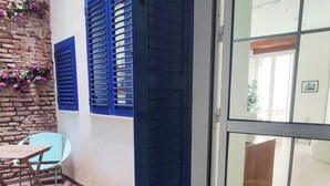A room with a wooden floor, a table with chairs, a blue shuttered window, and a glass door leading to an outdoor area. - Skyline Jacuzzi Living4malaga (Málaga)