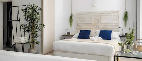 A modern bedroom with a large bed, bedside tables, a hanging light fixture, and a bathroom with a bathtub.