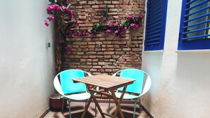 A small patio with a wooden table and two chairs, a brick wall with flowers, and a blue window shutter. - Skyline Jacuzzi Living4malaga (Málaga)