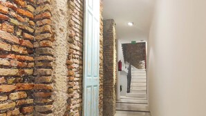 A corridor with exposed brick walls, a light blue door, and a staircase leading to a landing with a fire extinguisher. - Skyline Jacuzzi Living4malaga (Málaga)