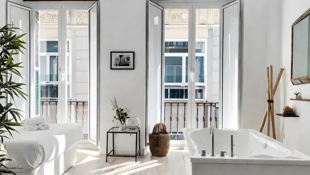 A modern hotel room with a large bathtub, a sofa, a small table with a vase, and a picture on the wall. - Skyline Jacuzzi Living4malaga (Málaga)